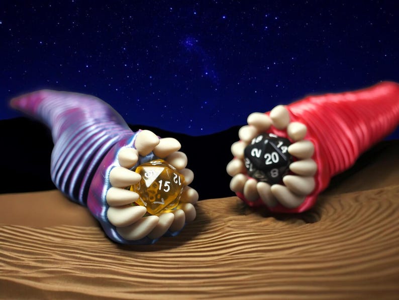 May include: Two fantasy-themed dice are held by stylized, tentacle-like forms. One die is yellow with the number 15 visible, the other is black with the number 20 visible. The background is a night sky with stars.