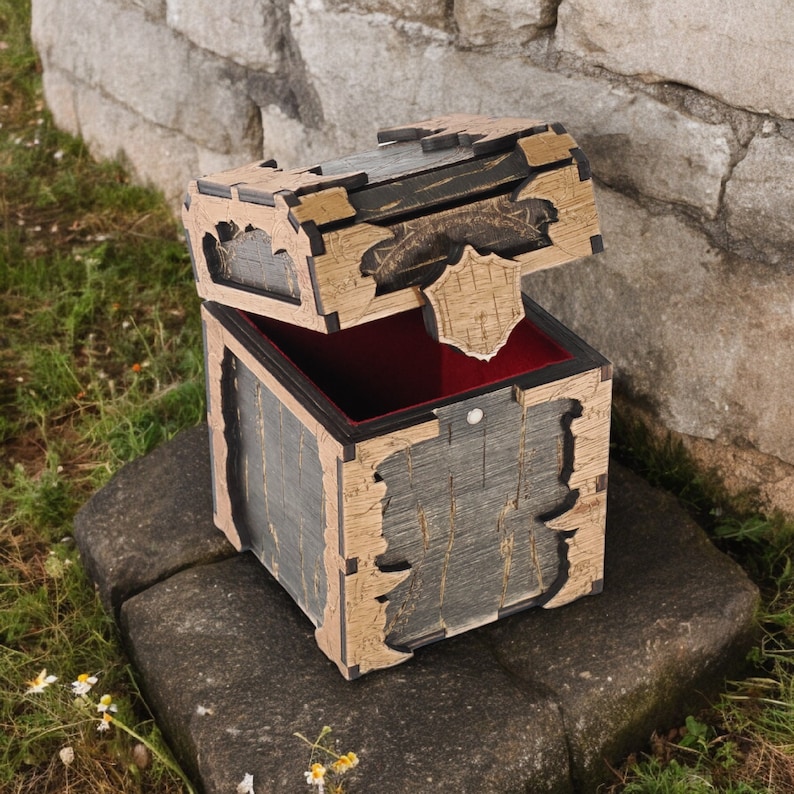 May include: A wooden treasure chest with a hinged lid, painted in distressed gray and tan. The interior is lined with red fabric. The chest is open, revealing the inside, and sits on a stone surface.