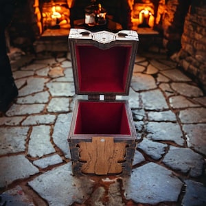 May include: Wooden treasure chest with an open lid, revealing a red velvet interior. The chest has intricate carved details and is set against a stone floor with a fireplace in the background. The chest is approximately 6 inches wide.