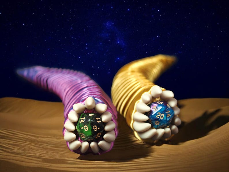 May include: Two stylized, worm-like creatures with dice in their mouths. One is purple, the other gold. Each holds a multi-sided die, one green, one blue. The background is a starry night sky over a desert.