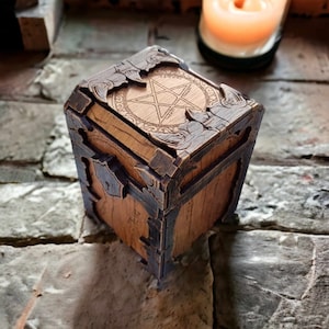 May include: A wooden box with a pentagram design on the lid. The box is brown with dark brown metal accents on the corners and edges. The box is sitting on a brick surface.