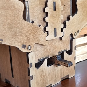 May include: A wooden puzzle box with intricate gear and lever mechanisms. The box is constructed from light brown wood with darker accents, showcasing a detailed design. The lever is in the shape of a sword.