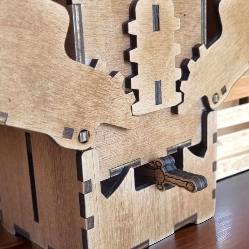May include: A wooden puzzle box with intricate gear and lever mechanisms. The box is constructed from light brown wood with darker accents, showcasing a detailed design. The lever is in the shape of a sword.