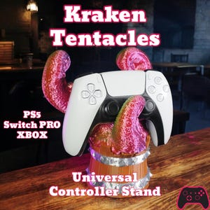 May include: A white and black game controller sits on a brown and silver universal controller stand. The stand features pink and red tentacles and the text "Kraken Tentacles" and "Universal Controller Stand". Compatible with PS5, Switch Pro, and Xbox consoles.