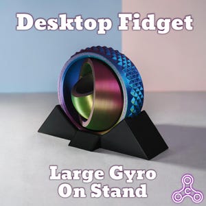 May include: A desktop fidget toy with a large gyro on a stand. The gyro has a blue, iridescent outer ring with a geometric pattern, and a multi-coloured inner sphere. The black stand holds the gyro upright. Text on the image reads "Desktop Fidget" and "Large Gyro On Stand."