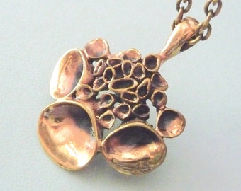 May include: A bronze pendant necklace with a unique design featuring multiple overlapping circles and a textured surface.