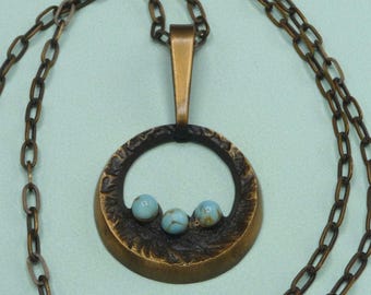 Peut inclure: Un collier avec un pendentif en bronze de forme circulaire orné de trois pierres turquoise. La chaîne est composée d'anneaux en bronze liés.
