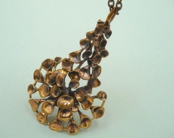 May include: A bronze pendant necklace with a delicate, intricate design resembling a cluster of leaves or flowers. The pendant is attached to a chain.