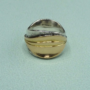 Könnte beinhalten: Ein Silber- und Goldring mit wellenförmigem Design. Der Ring besteht aus zwei Metallen, wobei der goldene Teil eine Wellenform auf dem Silber bildet.
