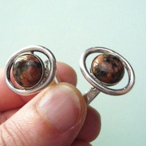 May include: A pair of silver earrings with a brown and black stone set in a circular design.