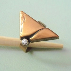 May include: A gold-toned ring with a triangular design and a single clear stone set in the center.