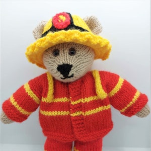 May include: A knitted teddy bear dressed as a firefighter. The bear is wearing a red and yellow striped jumpsuit, a yellow hat with a red circle, and black shoes.