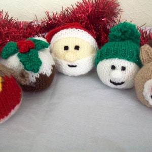 Puede incluir: Cinco adornos navide&ntilde;os de punto, incluyendo un mu&ntilde;eco de nieve, Pap&aacute; Noel, un petirrojo, un reno y un pud&iacute;n navide&ntilde;o. Los adornos son todos blancos con detalles de varios colores.