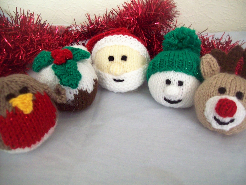 Puede incluir: Cinco adornos navide&ntilde;os de punto, incluyendo un mu&ntilde;eco de nieve, Pap&aacute; Noel, un petirrojo, un reno y un pud&iacute;n navide&ntilde;o. Los adornos son todos blancos con detalles de varios colores.