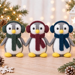 May include: Three handmade knit penguin plush toys standing side by side. Each penguin features a white belly, grey body, yellow beak, and yellow feet. They wear matching coloured earmuffs and scarves in dark green, deep red, and navy blue.