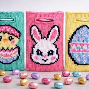 Puede incluir: Tres bolsas de regalo de Pascua tejidas en verde azulado, rosa y amarillo. Cada bolsa presenta un diseño diferente: un pollito saliendo de un huevo, una cara de conejito y un huevo decorado. Huevos de chocolate esparcidos delante.