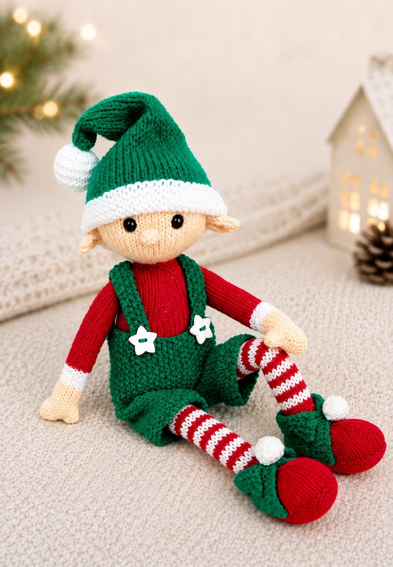 May include: A knitted elf doll featuring a green hat with a white pom-pom, a red long-sleeved shirt, and green overalls with two white star-shaped buttons. The doll has striped red and white legs, green shoes with white pom-poms, and beige skin.