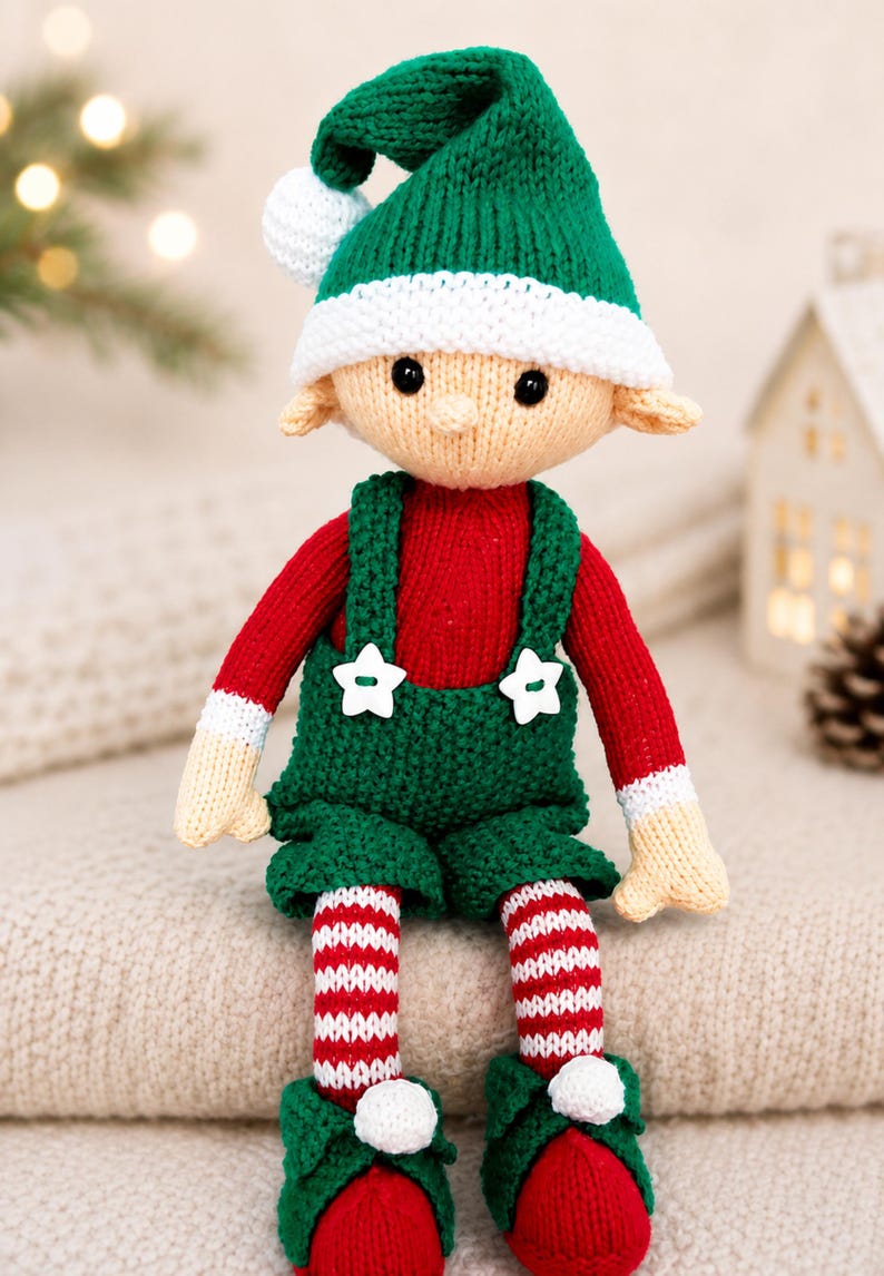 May include: A knitted elf doll featuring a green hat with a white pom-pom, a red long-sleeved shirt, and green overalls with two white star-shaped buttons. The doll has striped red and white legs and green shoes with white pom-poms at the toes.
