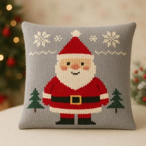 May include: A grey knitted cushion with a Santa Claus design. Santa is in a red suit, black belt, and white beard. Two green Christmas trees are either side of Santa, with snowflakes above.