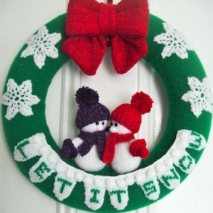Könnte beinhalten: Ein grüner, gestrickter Weihnachtskranz mit einer roten, gestrickten Schleife, zwei weißen, gestrickten Schneemännern mit lila und roten Mützen und weißen, gestrickten Schneeflocken. Der Kranz hat weiße, gestrickte Buchstaben, die "Let It Snow" buchstabieren.