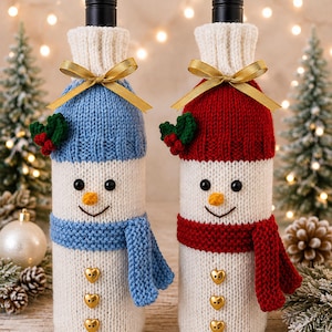 May include: Two knitted bottle covers shaped like snowmen, one with a blue hat and scarf and one with a red hat and scarf. Both feature white bodies, black button eyes, orange noses, three gold heart-shaped buttons, and a gold ribbon bow.