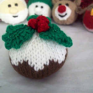 Puede incluir: Un adorno de pud&iacute;n navide&ntilde;o tejido con glaseado blanco, base marr&oacute;n y hojas de acebo verdes con bayas rojas.