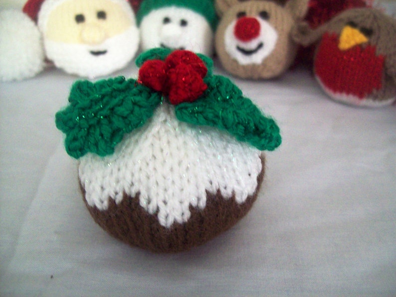 Puede incluir: Un adorno de pud&iacute;n navide&ntilde;o tejido con glaseado blanco, base marr&oacute;n y hojas de acebo verdes con bayas rojas.