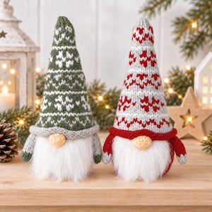 May include: Two plush gnome figurines with long white faux fur beards and round noses. One gnome wears a tall green and white knit hat with a snowflake pattern, while the other wears a tall red, white, and grey knit hat with a heart pattern.