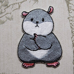May include: Embroidered iron-on patch of a grey hamster with a white belly and pink ears and feet. The hamster is standing with its arms crossed.