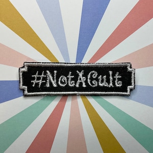 Könnte beinhalten: Schwarz-weiß gestickter Aufnäher mit dem Text "#NotACult" auf schwarzem Hintergrund.