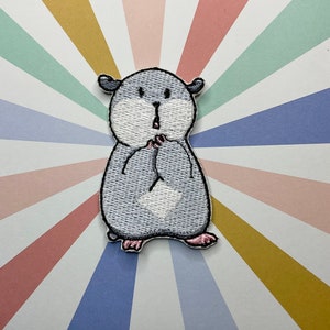 以下が含まれることがあります： 白いお腹とピンクの足を持つ、漫画のハムスターのグレーの刺繍アイロン接着パッチ。ハムスターは口を開けて驚いた表情をしていて、両手を顔に上げています。