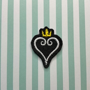 Peut inclure: Patch en forme de cœur noir avec un motif en spirale blanc et une couronne jaune sur le dessus.