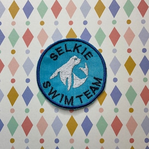 May include: A blue and white embroidered patch with the text "Selkie Swim Team" and a white silhouette of a seal.