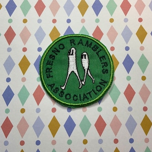 May include: A green embroidered patch with the text "FRESNO RAMBLERS ASSOCIATION" in a circular design. The patch features two white figures with legs. The patch is on a colorful diamond pattern background.