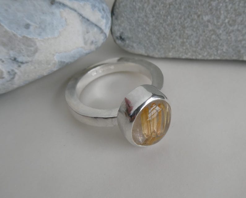 May include: A silver ring with a round, clear gemstone with gold inclusions. The gemstone is set in a silver bezel.