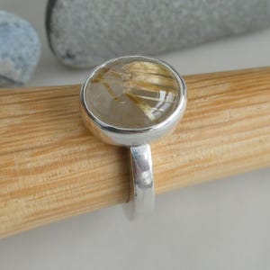 May include: A silver ring with a clear round stone containing gold flecks. The stone is set in a silver bezel.