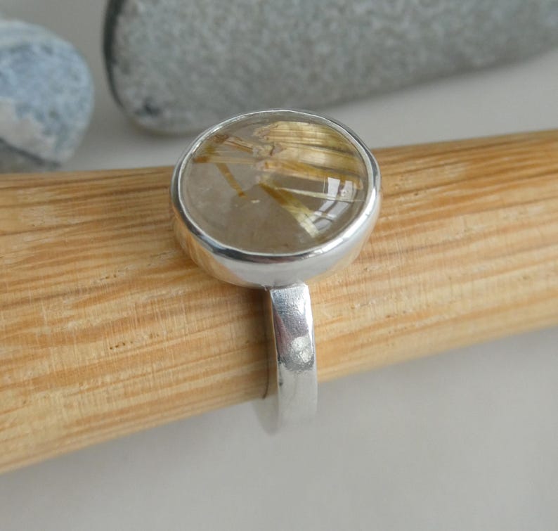 May include: A silver ring with a clear round stone containing gold flecks. The stone is set in a silver bezel.