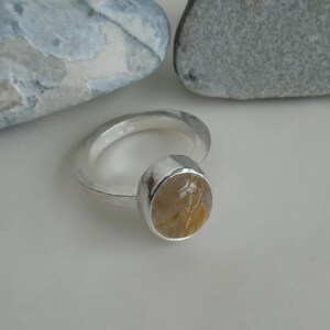 May include: A silver ring with a round, clear gemstone with gold flecks. The gemstone is set in a silver bezel.