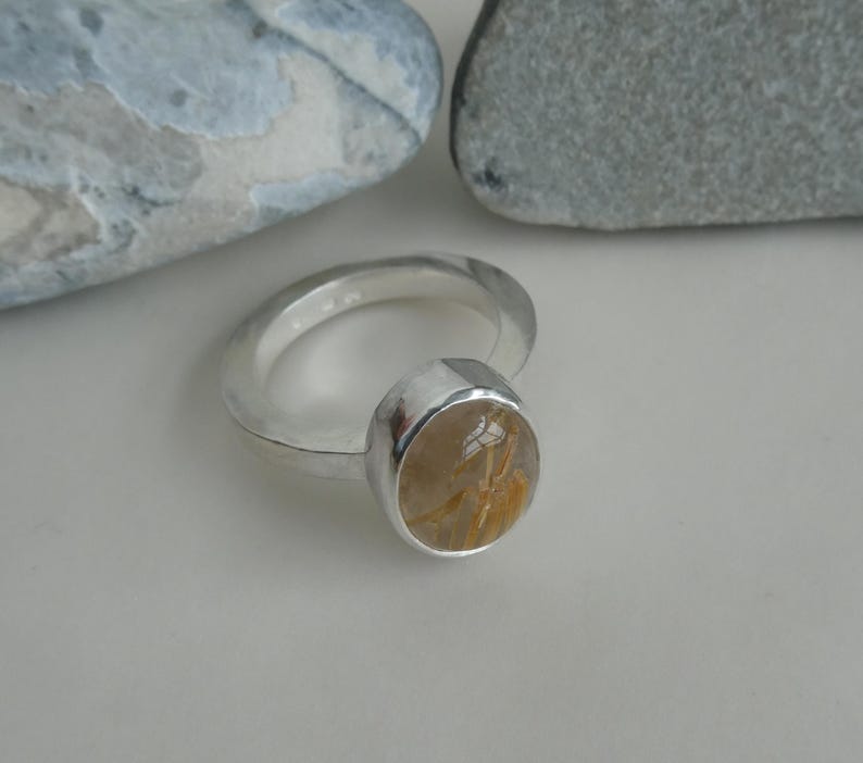 May include: A silver ring with a round, clear gemstone with gold flecks. The gemstone is set in a silver bezel.