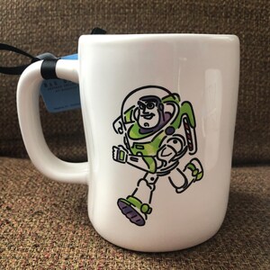 Puede incluir: Taza de cer&aacute;mica blanca con una imagen de dibujos animados de Buzz Lightyear de Toy Story corriendo. La taza tiene un asa negra.