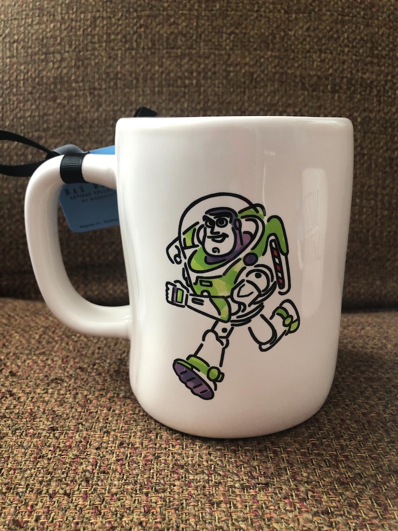 Puede incluir: Taza de cer&aacute;mica blanca con una imagen de dibujos animados de Buzz Lightyear de Toy Story corriendo. La taza tiene un asa negra.