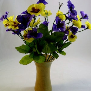 May include: A bouquet of purple and yellow pansies in a light brown ceramic vase. The flowers are arranged in a loose, natural style.