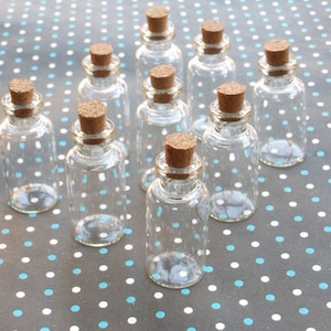 May include: Ten clear glass bottles with cork stoppers. The bottles are arranged in a triangular pattern on a gray and white polka dot surface.