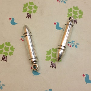 May include: Two silver bullet-shaped charms with a loop at the top for attaching to a necklace or bracelet.