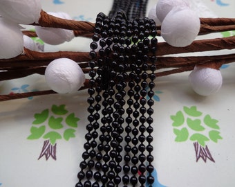 Puede incluir: Cadena negra con cuentas redondas. La cadena es de metal y tiene aproximadamente 4 mm de ancho. La cadena está sobre una superficie blanca con un patrón floral.