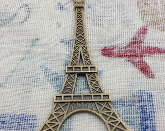 Puede incluir: Un amuleto de color bronce en forma de Torre Eiffel con un diseño detallado. El amuleto tiene un bucle en la parte superior para sujetarlo a un collar o pulsera.