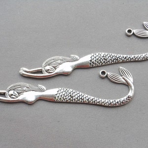 May include: Two silver mermaid bookmark charms with a detailed design. Each charm features a mermaid with flowing hair and a scaly tail.
