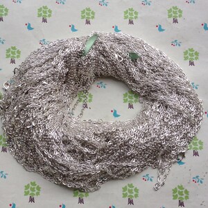 May include: A large pile of silver chain, likely for jewelry making, is shown on a patterned background.