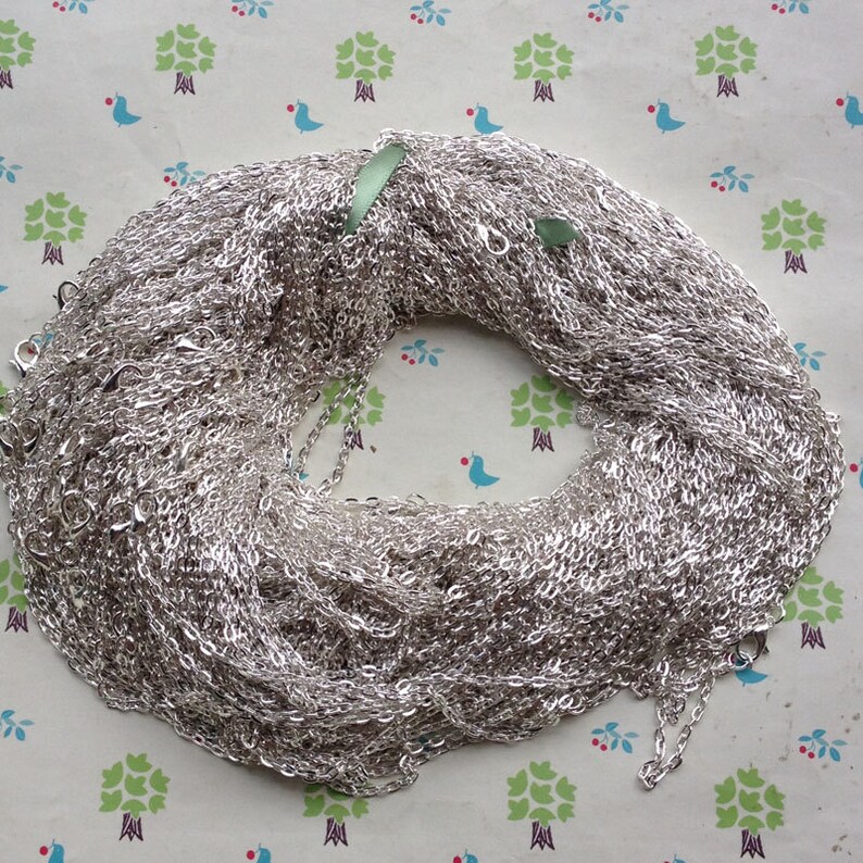 May include: A large pile of silver chain, likely for jewelry making, is shown on a patterned background.