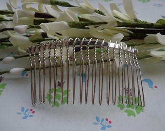 May include: A silver hair comb with a curved, twisted wire design and multiple teeth. The comb is lying on a white surface with a floral pattern.